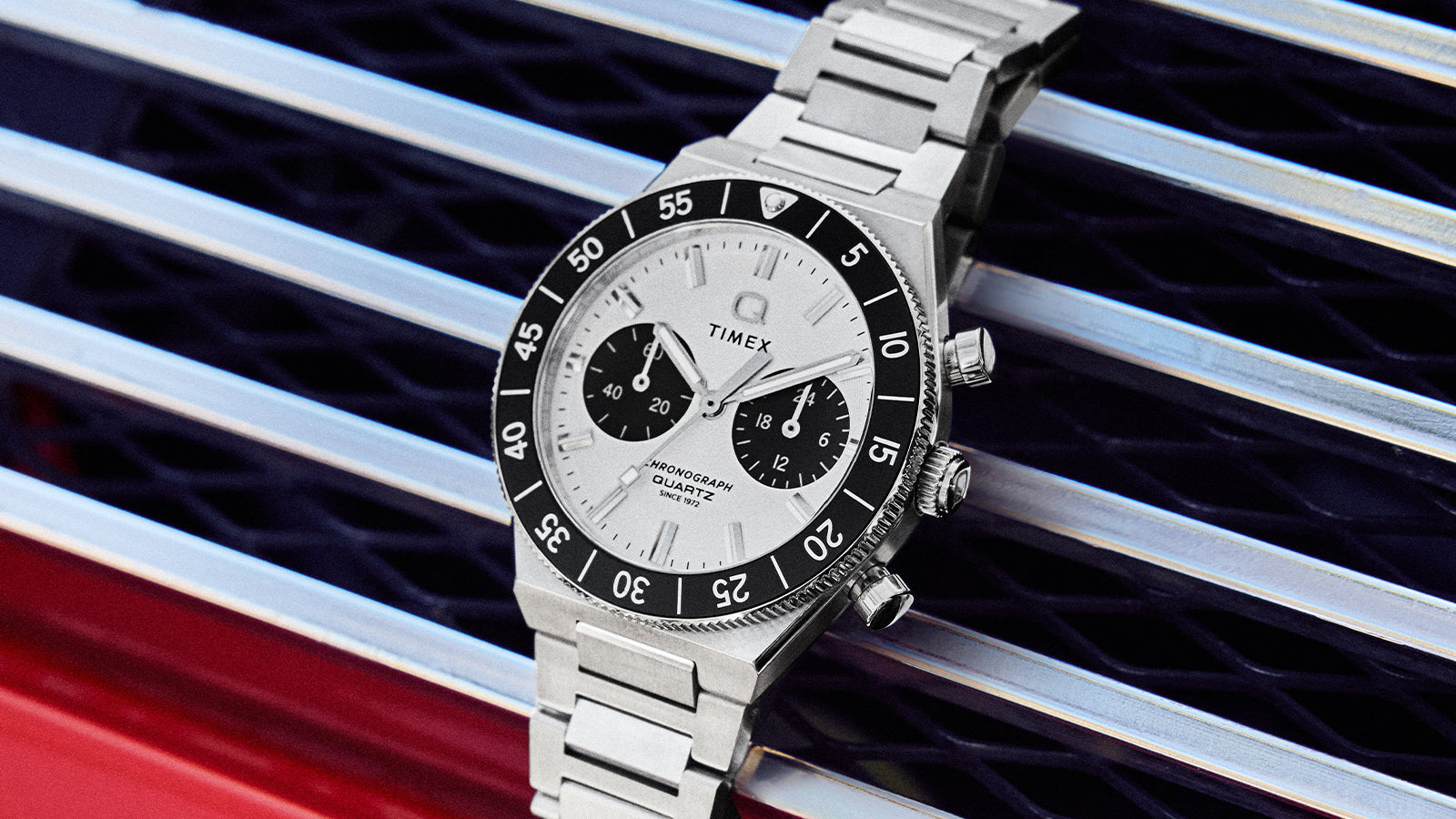 Angled view of the Q Timex Continental Chronograph showing the silver dial, black unidirectional bezel, and stainless steel bracelet.