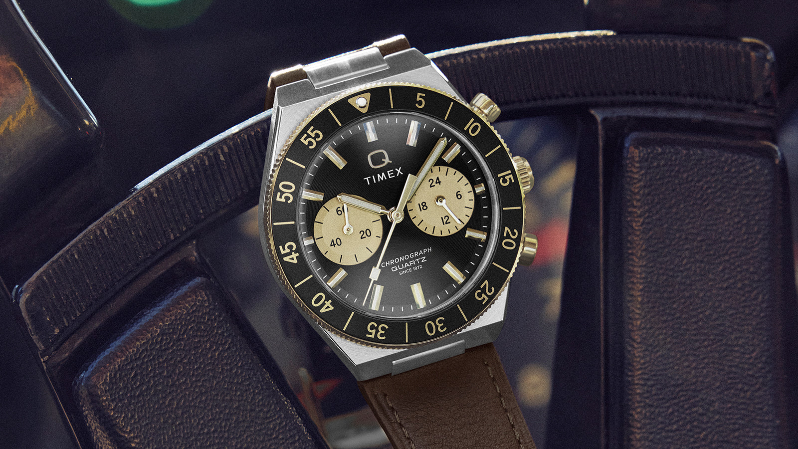 Q Timex® Continental Chronograph watch resting on a vintage car steering wheel, featuring a black dial with champagne subdials and brown leather strap.