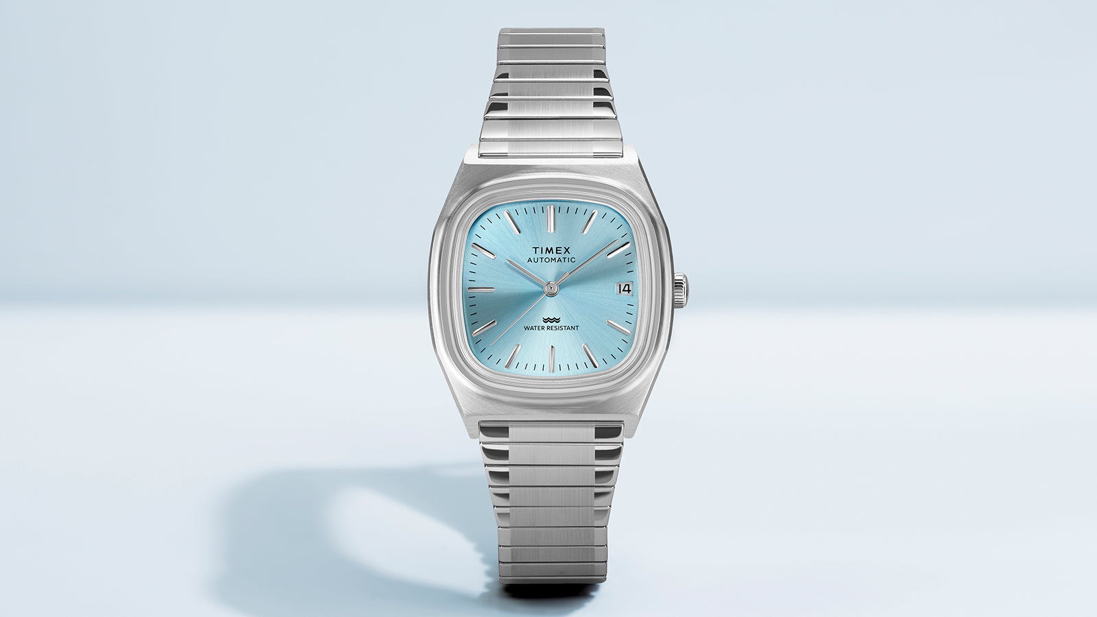 Timex® Automatic 1983 E Line watch shown straight-on with a light blue sunray dial, date display, and stainless steel expansion bracelet.