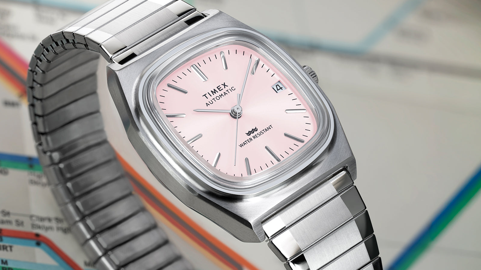 Close-up of the Timex® Automatic 1983 E Line watch emphasizing the brushed stainless steel case, pink dial, and expansion bracelet.