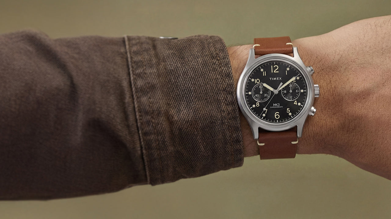 Side view of Timex MK1 Chronograph on wrist with brown leather strap and black dial with luminous Arabic numerals.