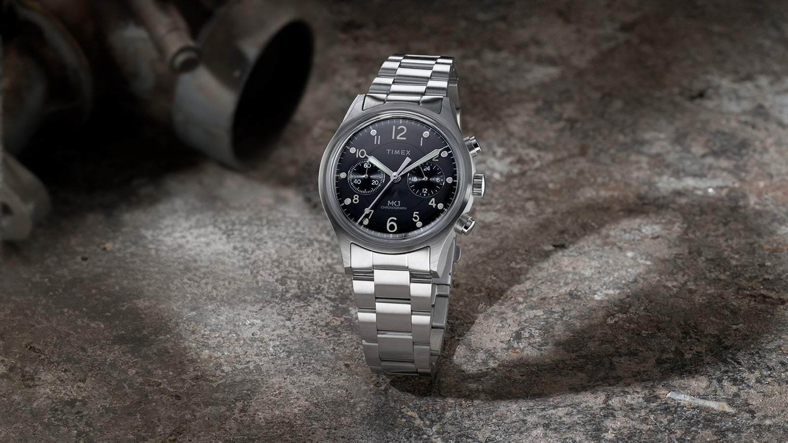 Timex MK1 Chronograph stainless steel watch displayed on a stone surface, highlighting the black dial and chronograph pushers.
