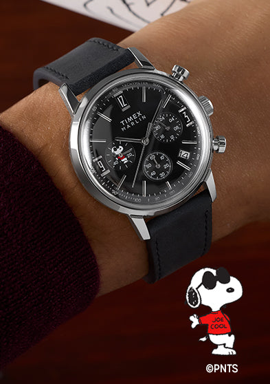 Peanuts® x Timex Marlin® Chronograph Joe Cool watch worn on a wrist, featuring a stainless steel case, black leather strap, black chronograph dial, and Snoopy as Joe Cool in a red shirt on a subdial.