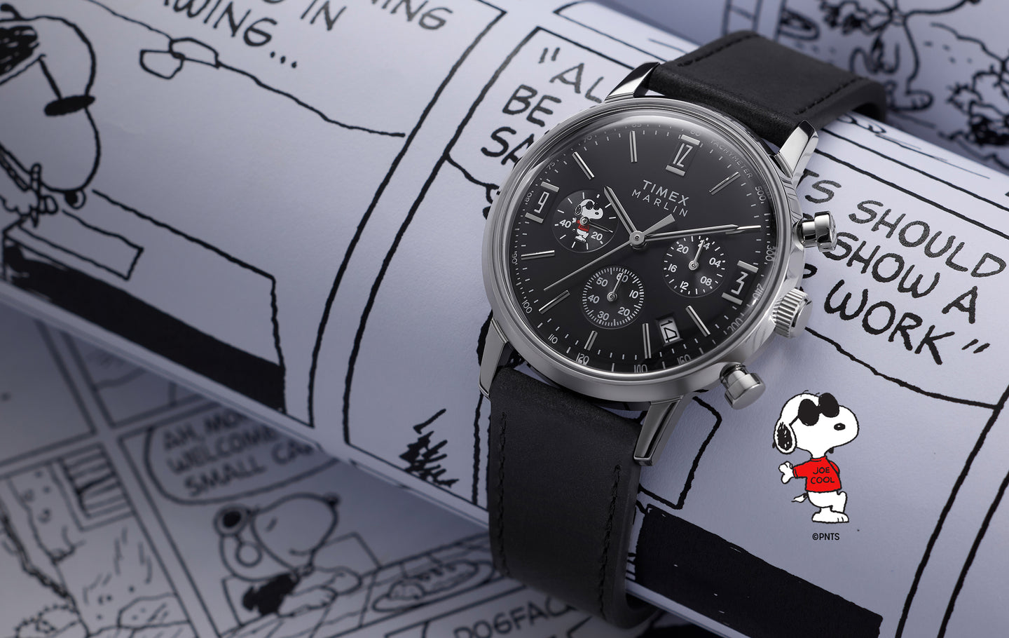 Peanuts® x Timex Marlin® Chronograph with black dial and black leather strap, featuring Snoopy in the subdial, displayed on a Peanuts comic strip background with Joe Cool illustrated in a red shirt.