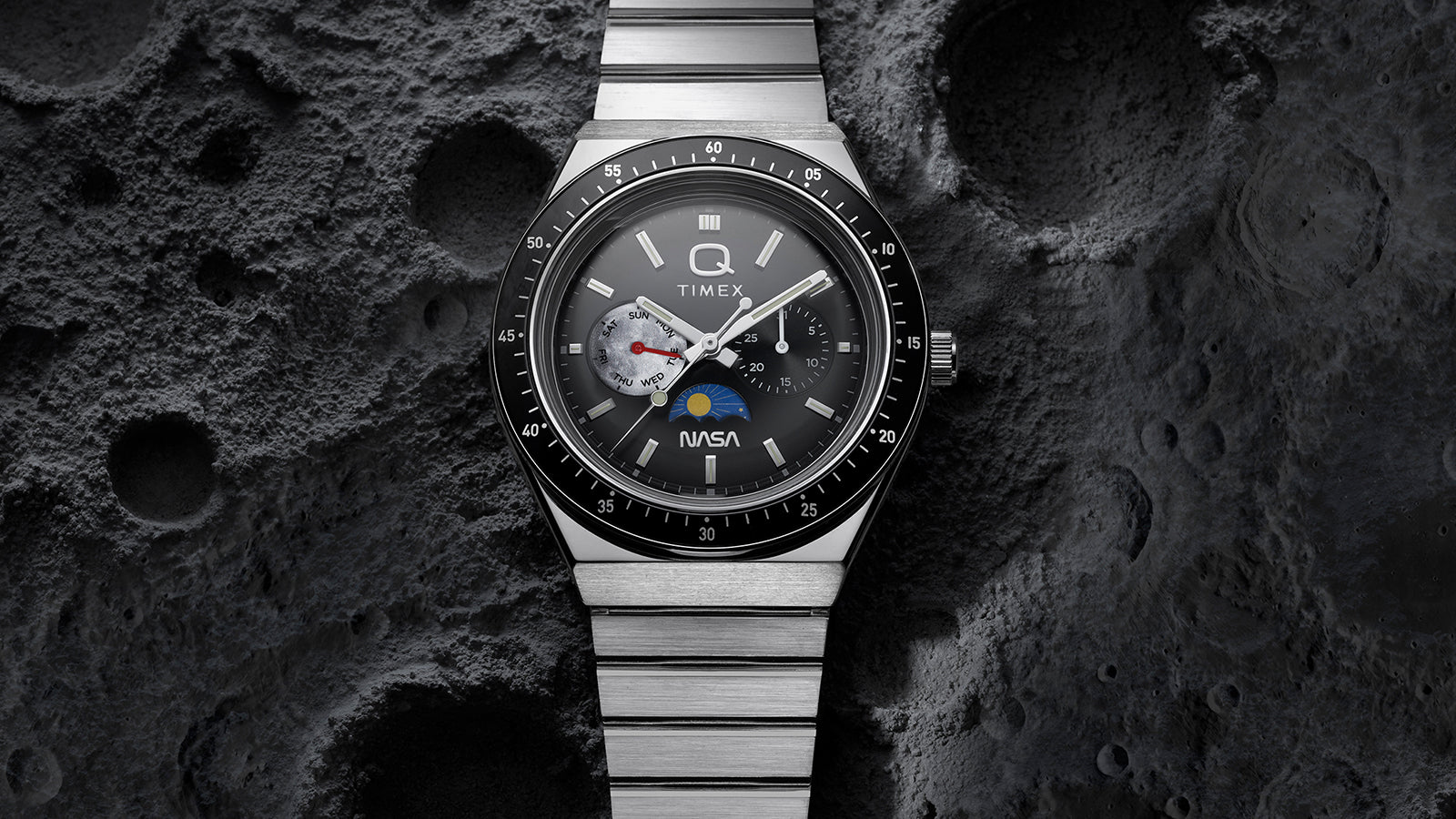 Front view of Q Timex® x NASA stainless steel watch with black bezel and gray dial set against a cratered moon-inspired surface.