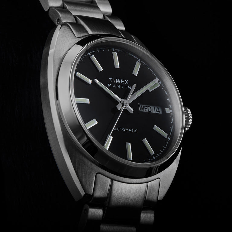 Close-up of the Timex Marlin Draper Automatic black dial with luminous hour markers, silver hands, and day-date display.