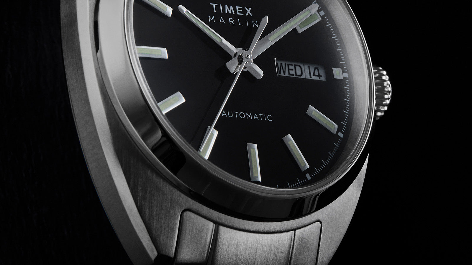 Close-up of the Timex Marlin Draper Automatic black dial with luminous hour markers, silver hands, and day-date display.