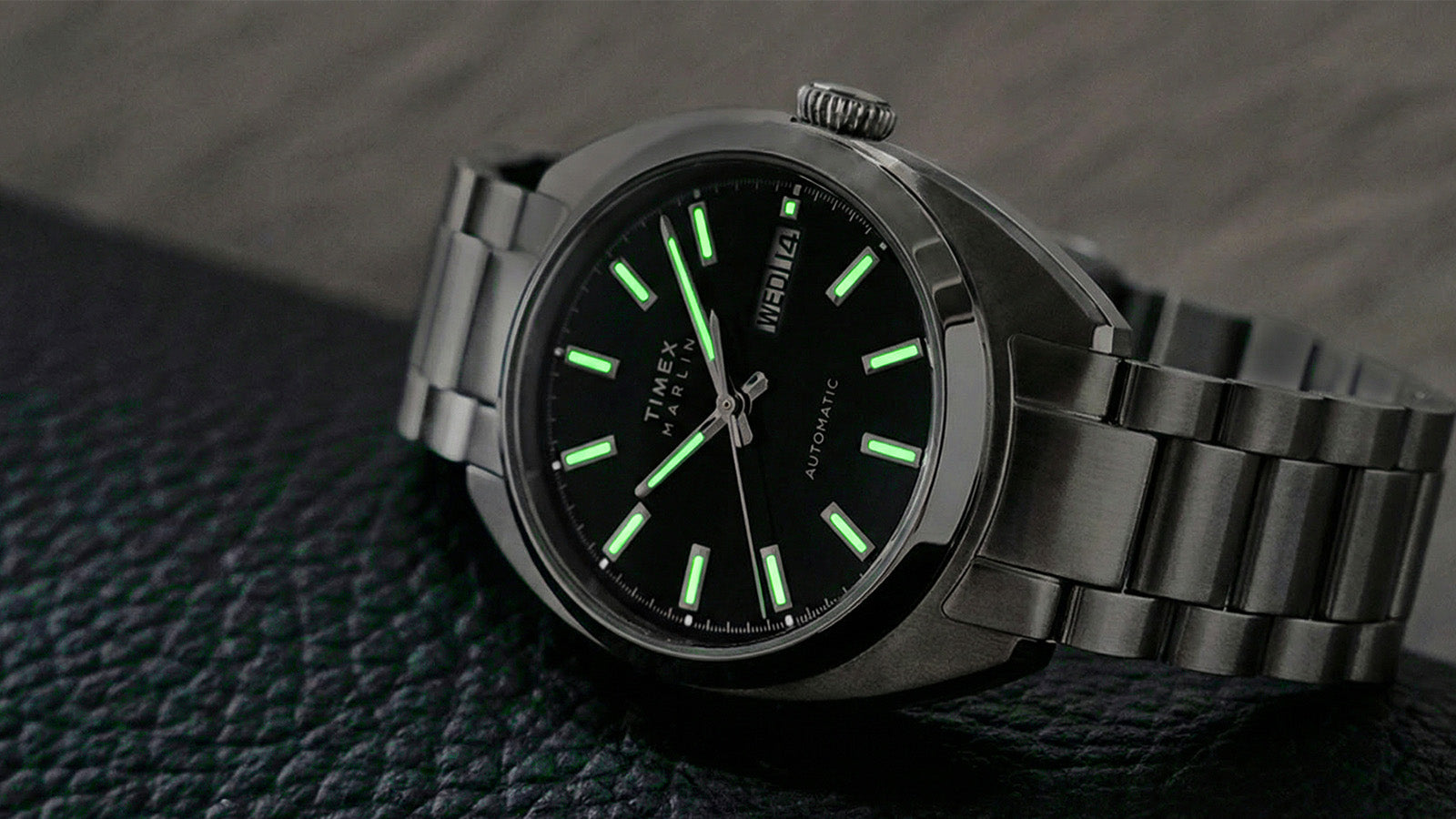 Timex Marlin Draper Automatic watch with green-glowing luminous hour markers and hands in low light.
