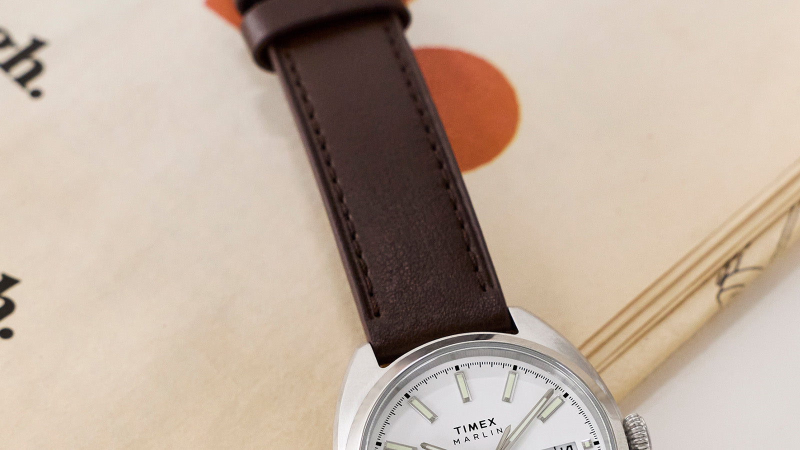 Detail view of the Timex Marlin® Draper Automatic brown leather strap and stainless steel case resting on a book.