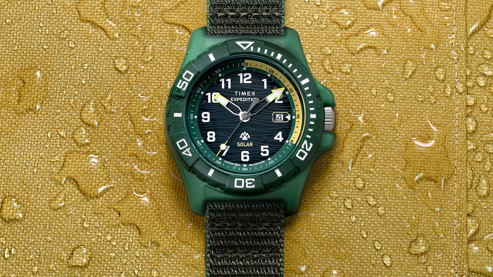 Front view of Timex Expedition® Freedive Solar watch centered on yellow textured surface with visible water droplets and black fabric strap.