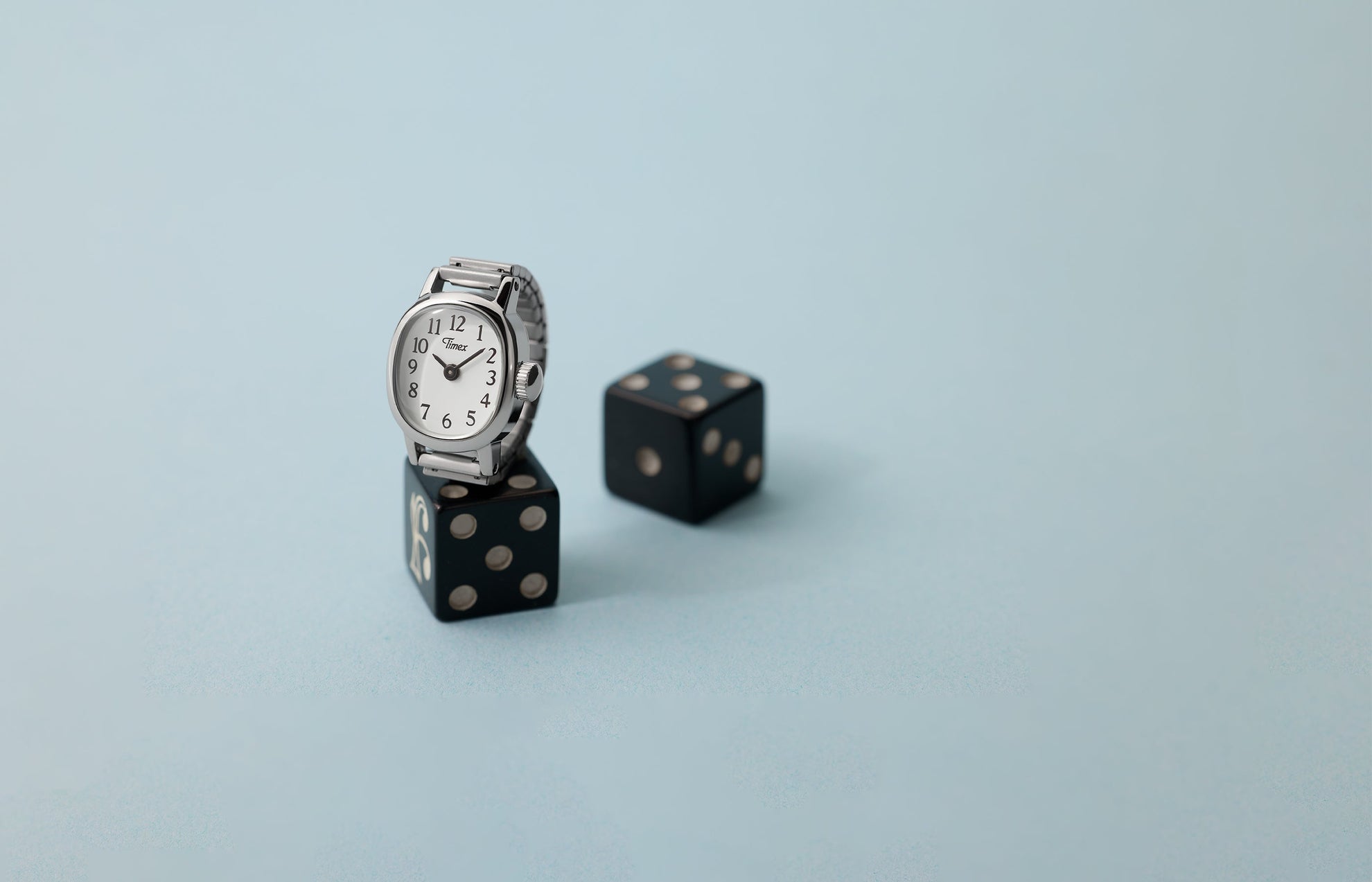 Timex Cavatina® Mini silver-tone watch with white dial displayed on black dice against soft blue background.