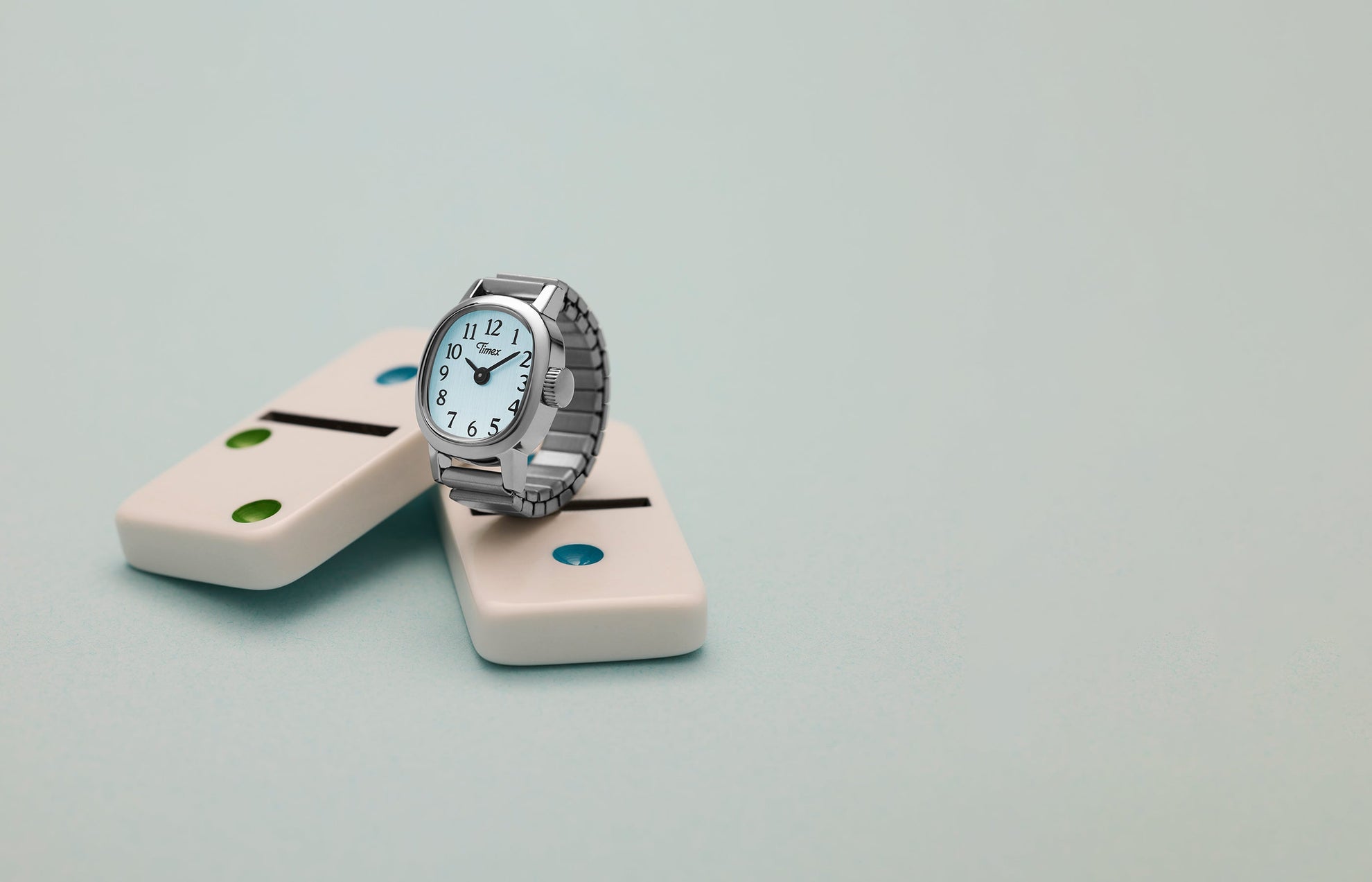 Timex Cavatina® Mini silver-tone watch displayed on white domino blocks against soft blue background.