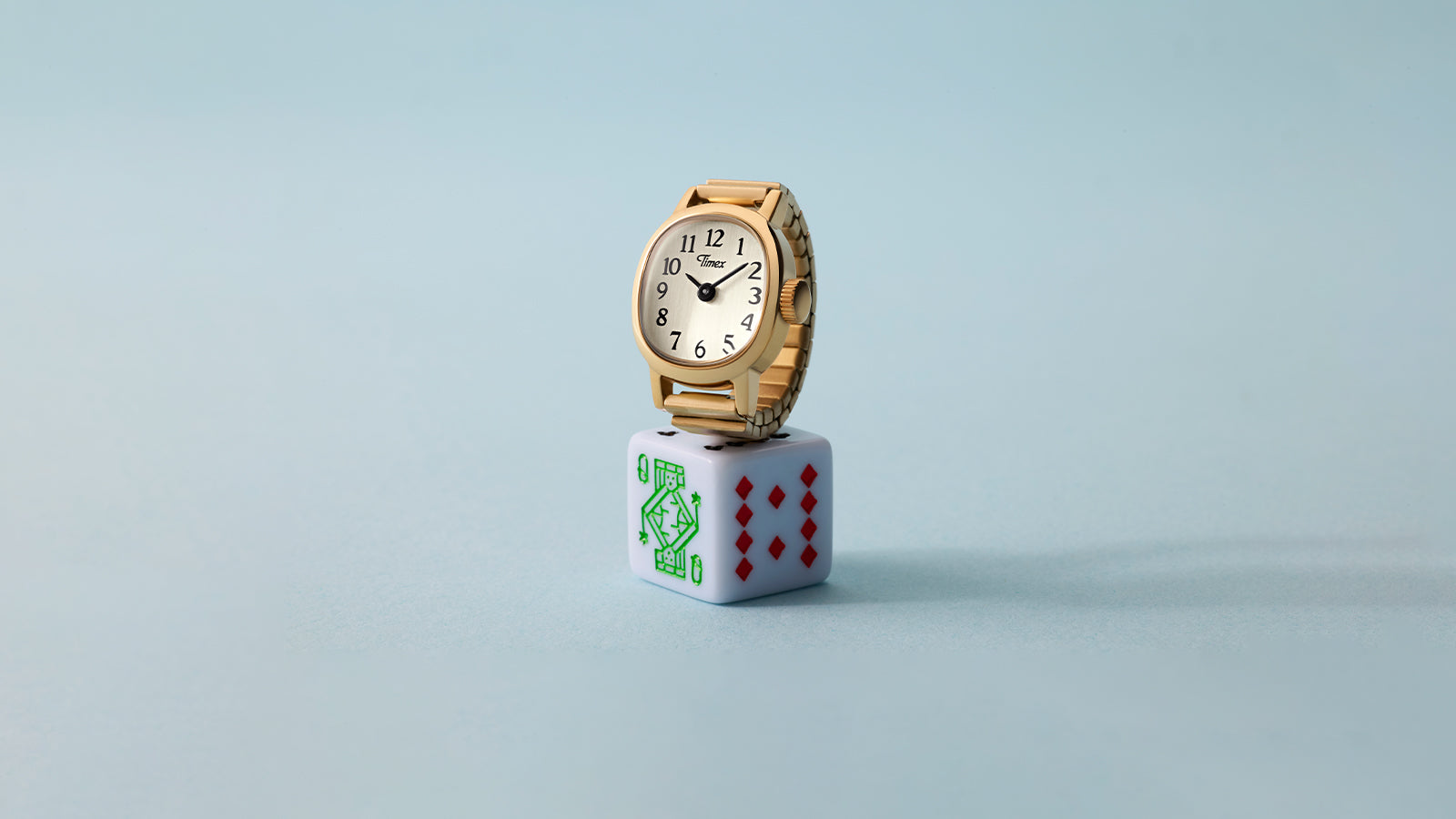 Timex Cavatina® Mini gold-tone watch with champagne dial displayed on white playing die against soft blue background.