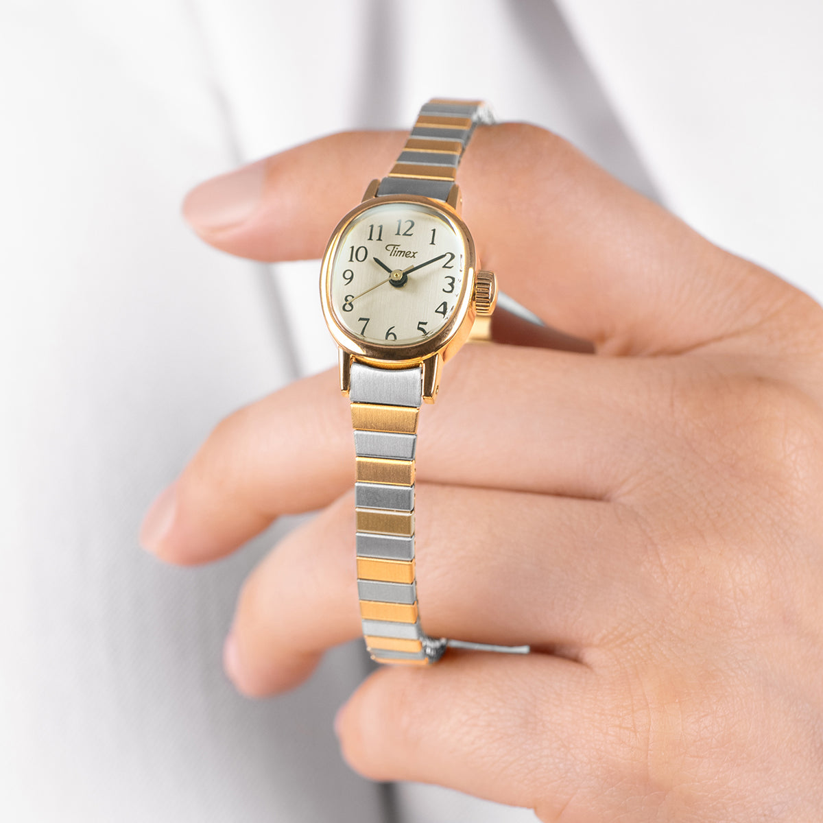 Cavatina® Mini women’s watch with gold-tone oval case and two-tone expansion bracelet worn on wrist, showing cream dial with Arabic numerals.