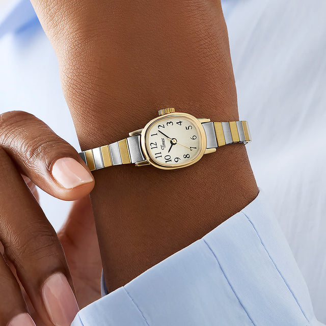 Cavatina® Mini women’s watch with gold-tone case and two-tone stainless steel bracelet worn on wrist, featuring a cream dial and black Arabic numerals.