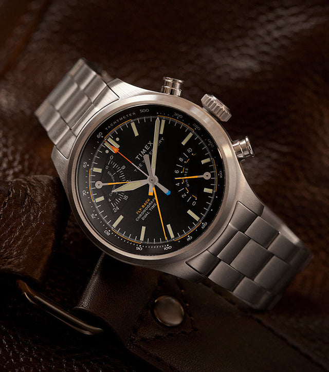 Timex Waterbury Ace Fly-Back Chronograph with black dial and stainless steel bracelet resting on brown leather bag