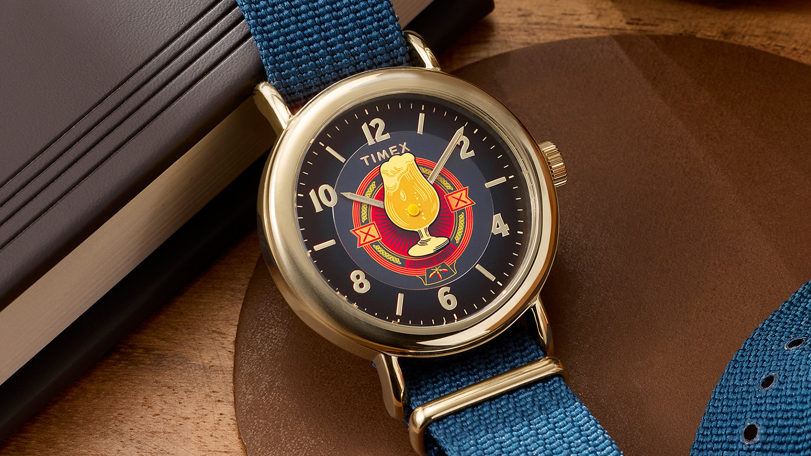 Harry Potter x Timex Weekender Butterbeer watch with blue fabric strap resting on tabletop with books.