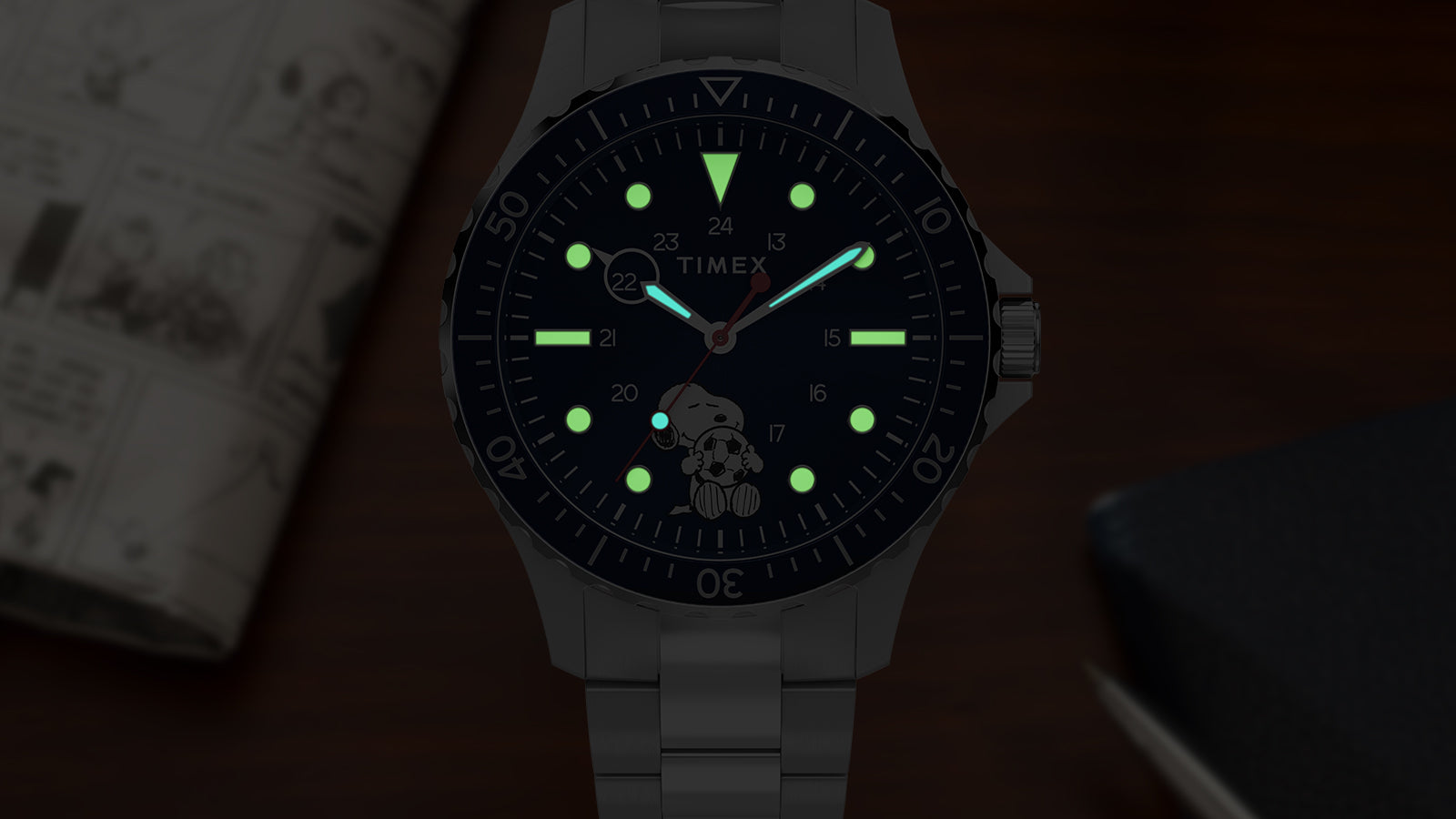 Close-up of Timex Navi Snoopy soccer watch dial glowing with luminous hour markers and hands in low light