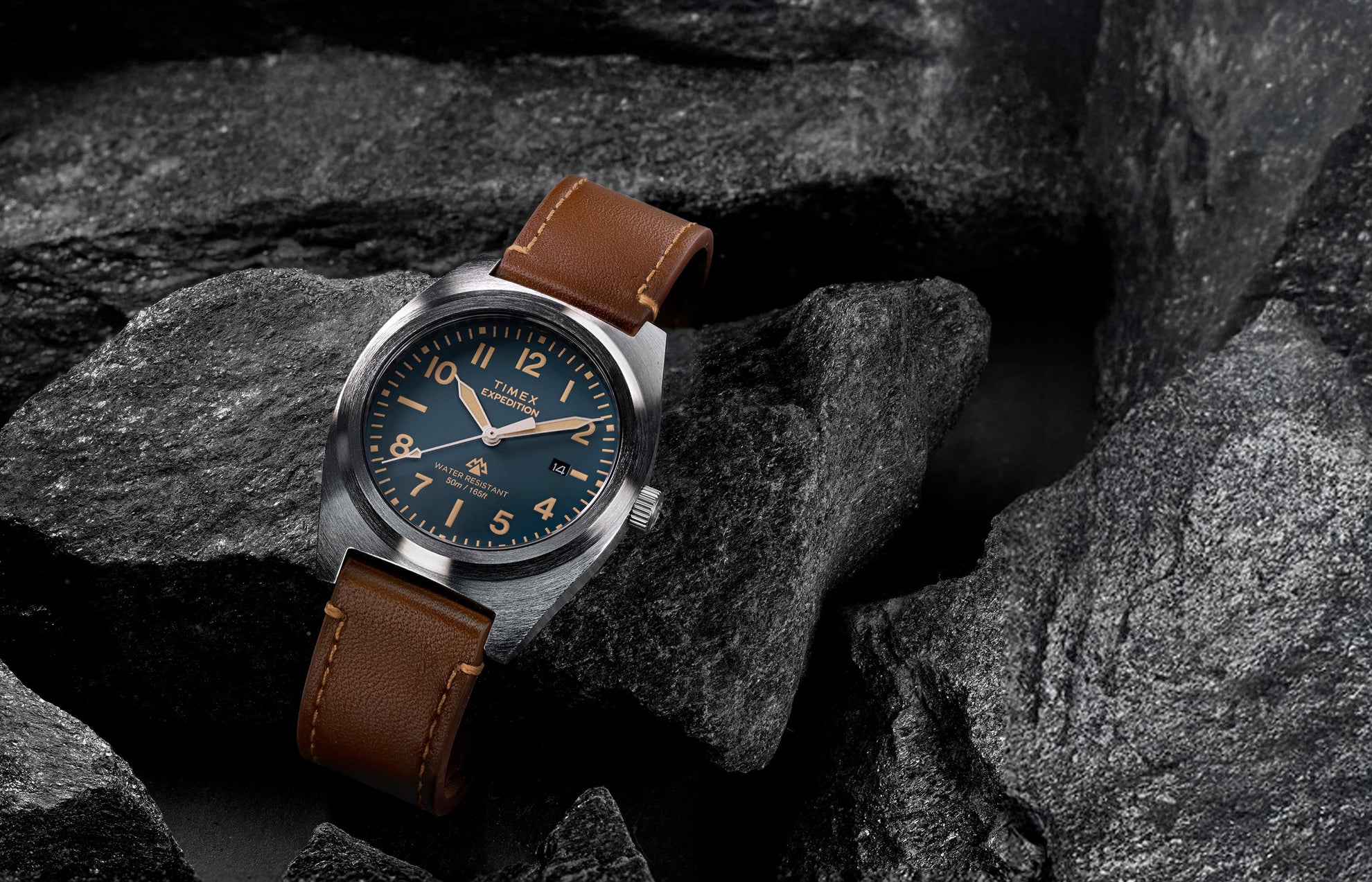 Timex Expedition Capstone watch with blue dial and brown leather strap resting on rocks