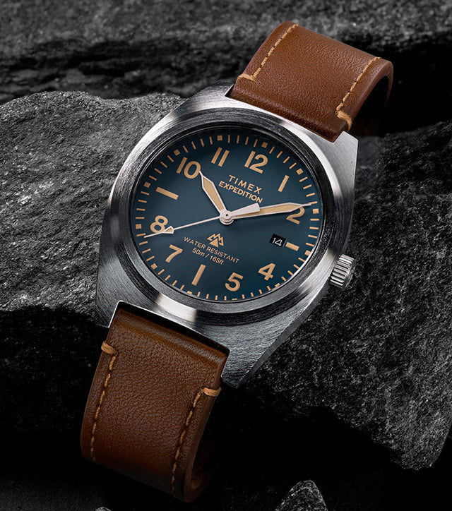 Timex Expedition Capstone watch with blue dial and brown leather strap resting on rocks
