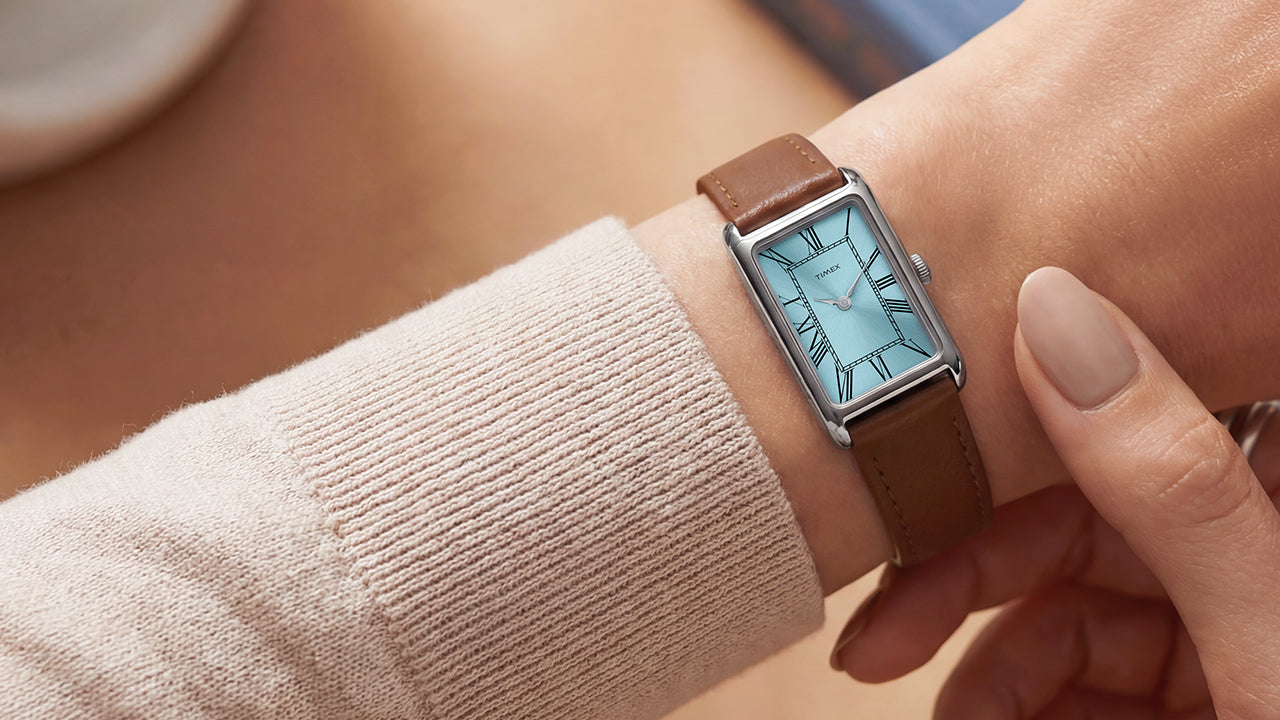 Person wearing the Timex® 1976 Lexington Reissue Inspired watch featuring a rectangular silver-tone case, light blue dial with Roman numerals, and brown leather strap.