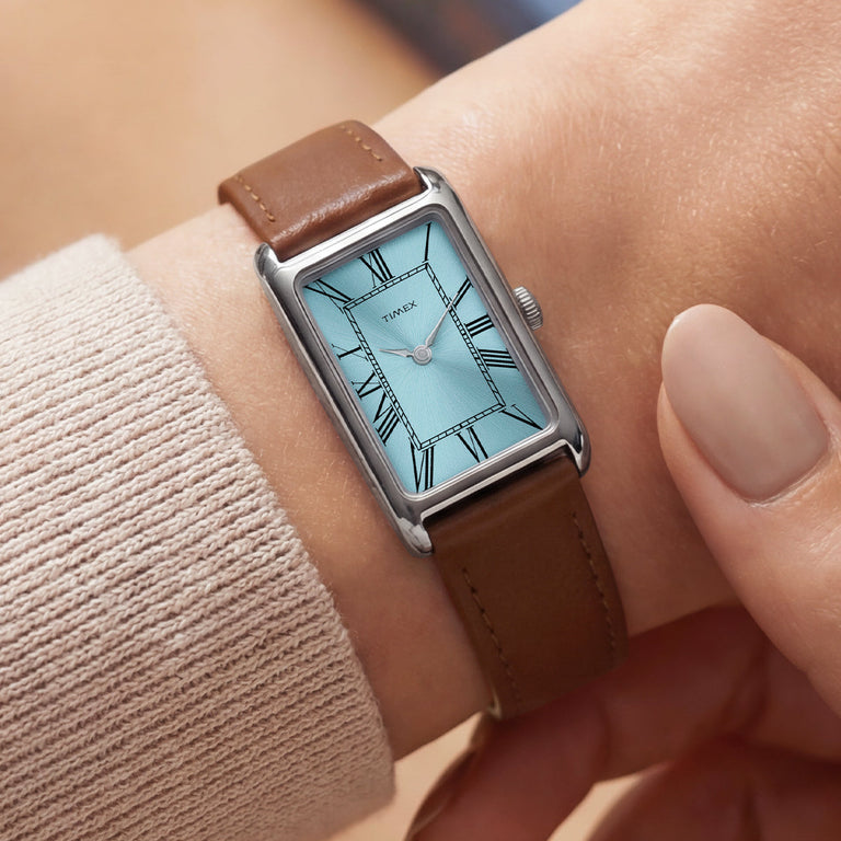Close-up view of the Timex® 1976 Lexington Reissue Inspired watch on a wrist, highlighting the light blue dial, Roman numerals, and brown leather strap.