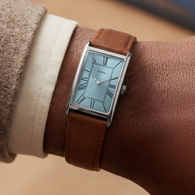 Timex® 1976 Lexington Reissue Inspired watch worn on a wrist, showcasing its rectangular silver-tone case, light blue dial, and brown leather strap.
