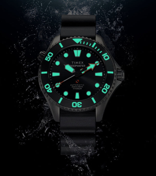 Timex Deepwater Meridian 300 Titanium HEV Automatic dive watch displaying bright blue-green Super-LumiNova illumination against a dark underwater-inspired background.