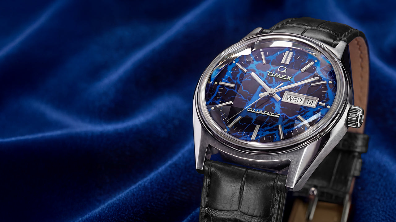 Angled hero shot of Q Timex Blue Vega quartz watch featuring brushed stainless steel case, blue lightning dial, and black crocodile-grain leather strap