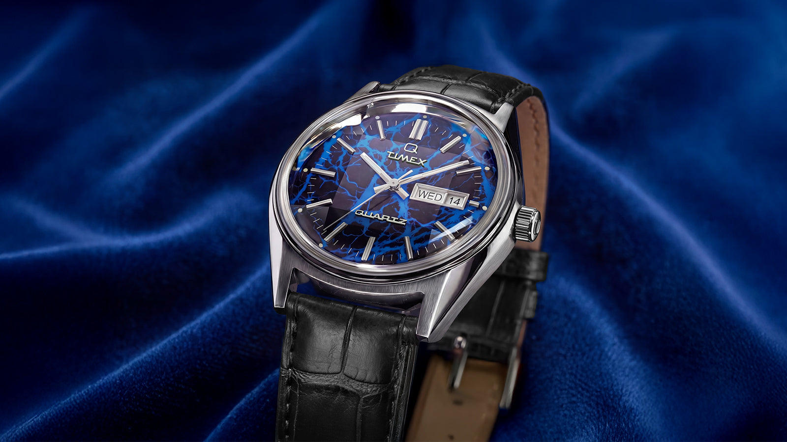 Angled hero shot of Q Timex Blue Vega quartz watch featuring brushed stainless steel case, blue lightning dial, and black crocodile-grain leather strap