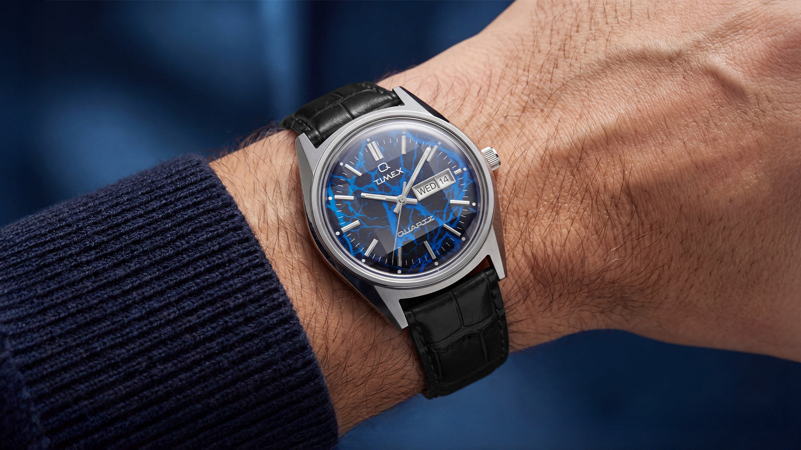 Lifestyle wrist shot of Q Timex Blue Vega watch paired with navy knit sleeve and black leather strap