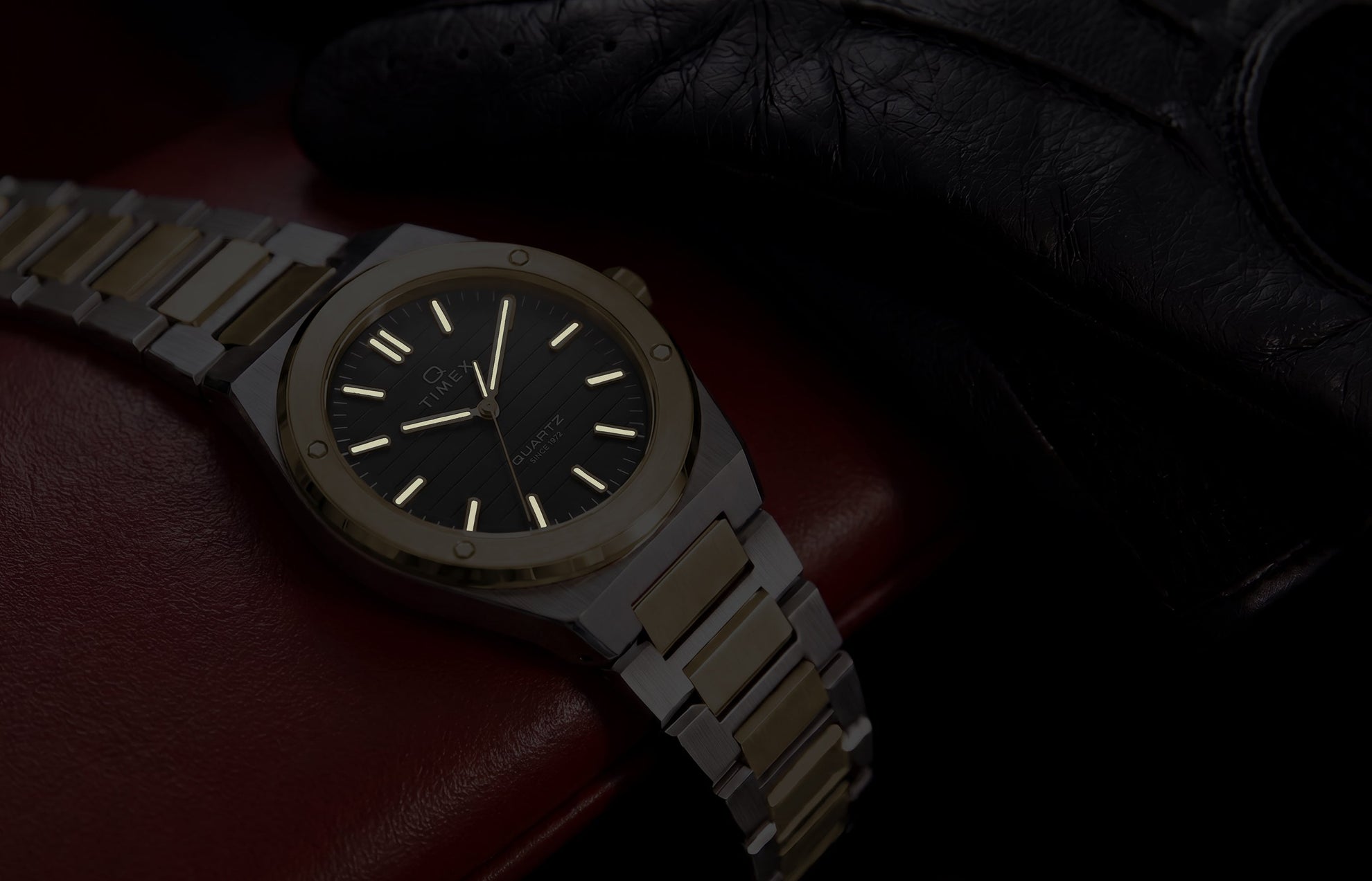 Timex Q Marbella two-tone watch with illuminated hands and hour markers shown on a red leather car seat in low light.