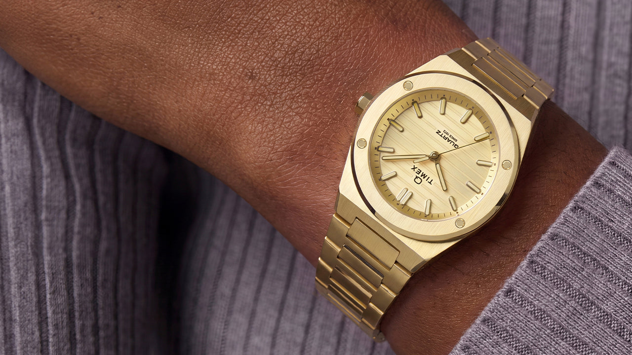 Q Timex Marbella gold-tone stainless steel watch with a champagne dial and integrated bracelet worn on the wrist.