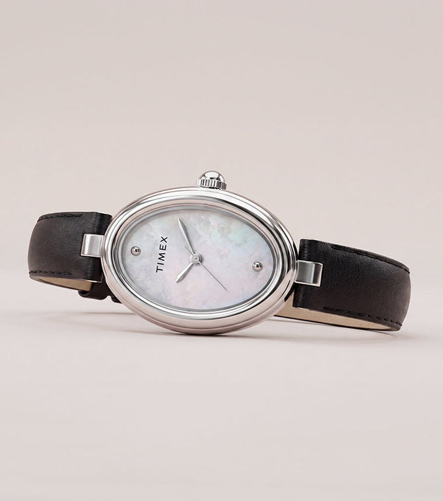 Timex Cavatina® Luxe watch with a silver-tone oval case, mother-of-pearl dial, and black leather strap displayed on a soft neutral background.