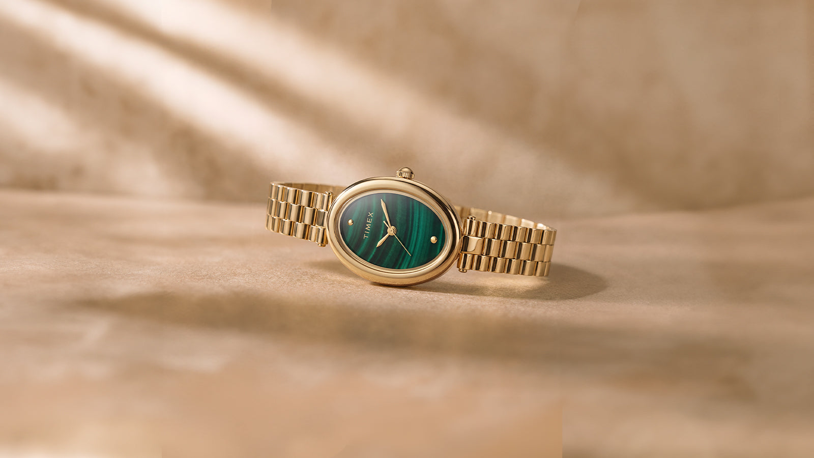 Timex Cavatina® Luxe gold-tone watch with a green malachite-pattern dial displayed on a warm neutral surface in soft natural light.
