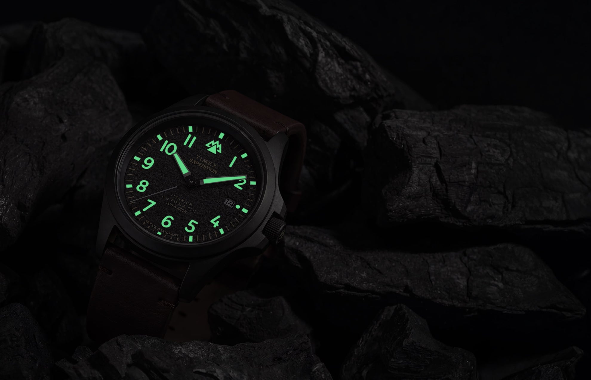 Expedition® Field Post Automatic titanium watch with glowing luminous hands and hour markers in low light.