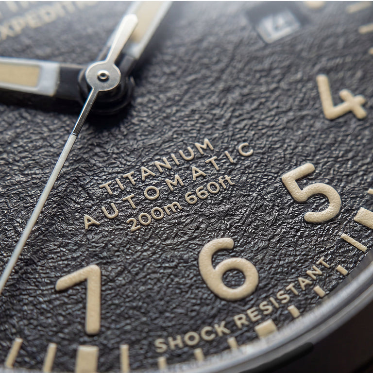 Close-up of the Expedition® Field Post Automatic textured black dial showing automatic movement, 200m water resistance, and shock resistance.