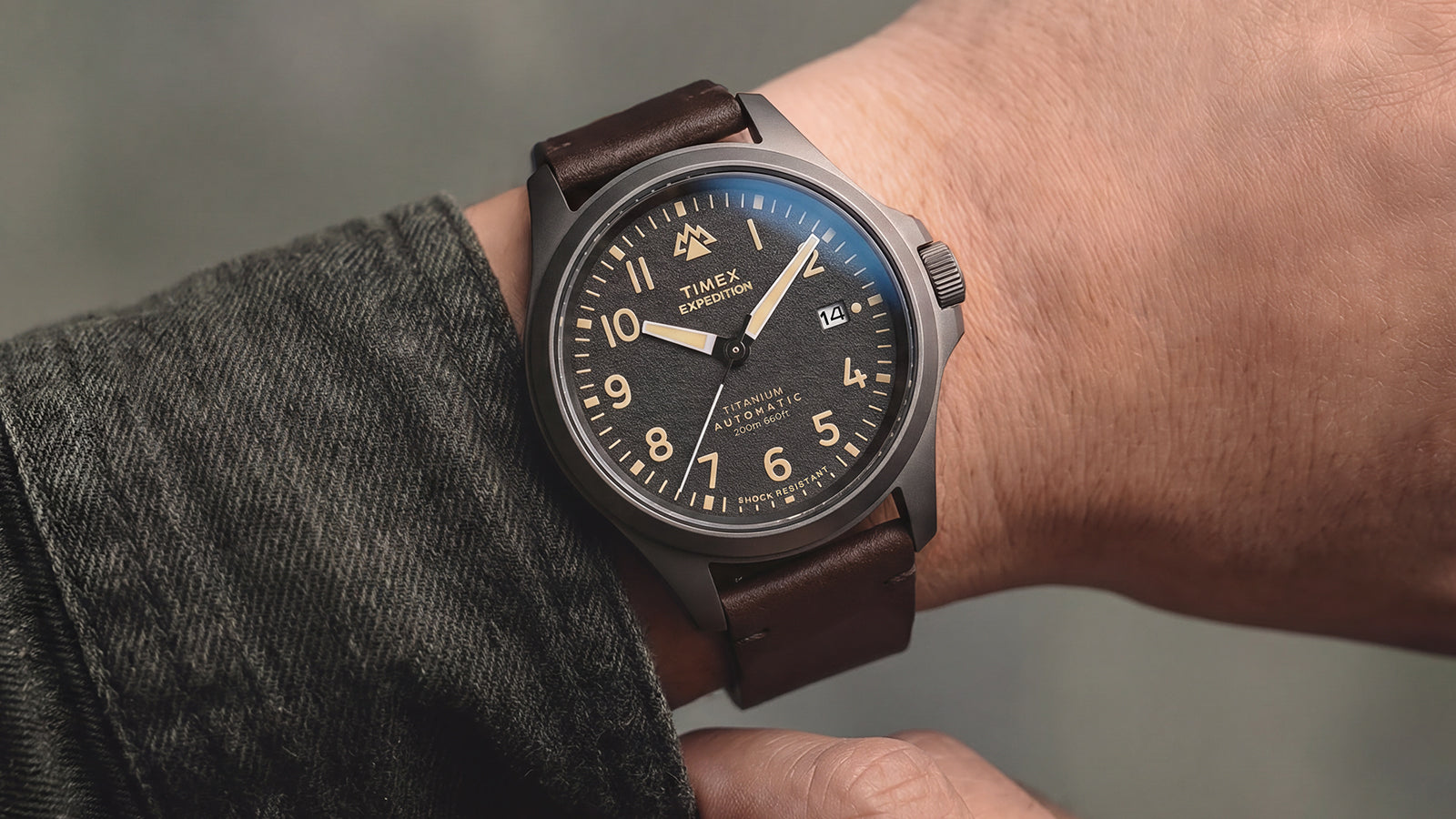 Expedition® Field Post Automatic titanium watch with a black dial and brown leather strap worn on the wrist.