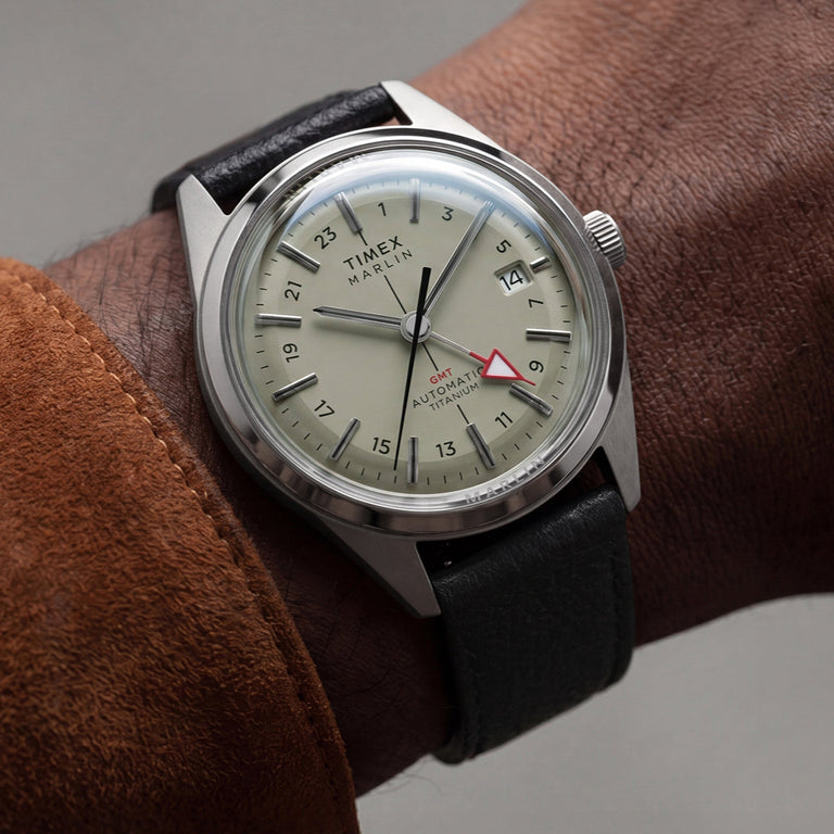 Timex Marlin® Jet Titanium Automatic GMT worn on wrist, featuring a lightweight titanium case, cream dial, red GMT hand, and black leather strap.