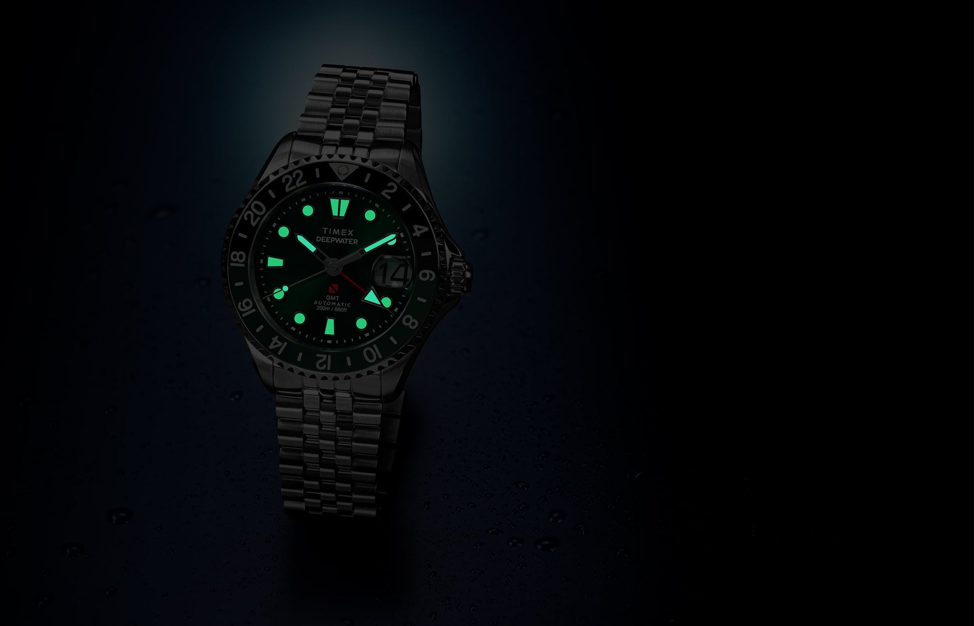 Timex Deepwater Meridian 200 Automatic GMT watch with a green dial and glowing luminous hands and hour markers, displayed against a dark blue background with water droplets.