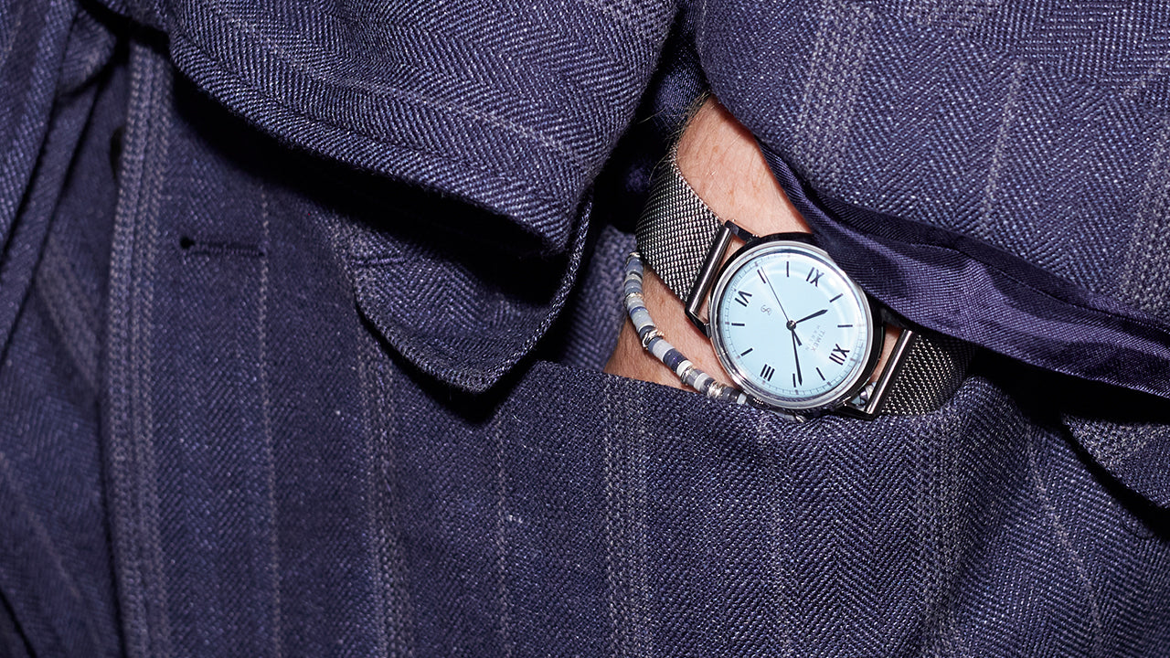 Todd Snyder x Timex Marlin® Mesh watch with a light blue dial tucked into the pocket of a navy pinstripe blazer, paired with beaded bracelets.
