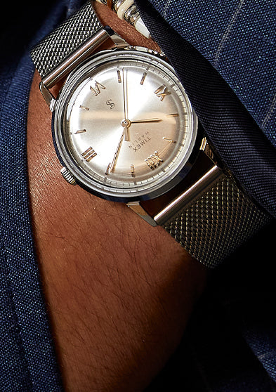 Todd Snyder x Timex Marlin® Mesh watch with a silver sunray dial worn beneath the cuff of a navy pinstripe suit jacket.