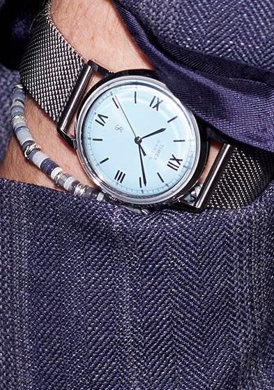 Todd Snyder x Timex Marlin® Mesh watch with a light blue dial tucked into the pocket of a navy pinstripe blazer, paired with beaded bracelets.