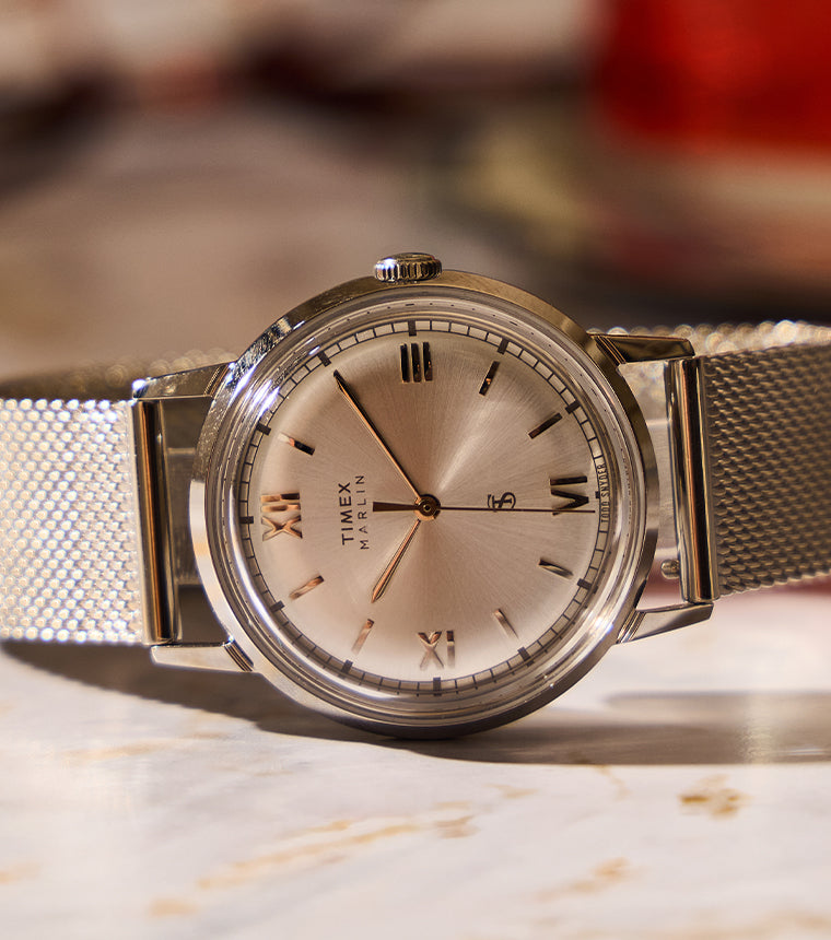 Todd Snyder x Timex Marlin® Mesh watch with a silver sunray dial and stainless steel mesh bracelet displayed on a marble table.