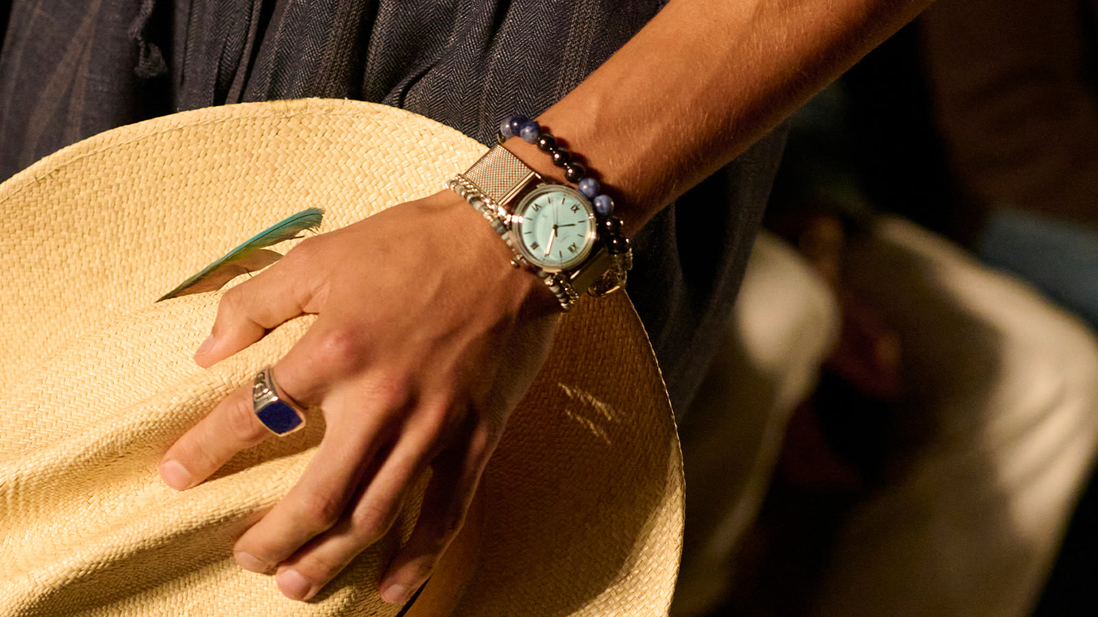 Todd Snyder x Timex Marlin® Mesh watch with a light blue dial and stainless steel mesh bracelet worn with layered bracelets while holding a straw hat.
