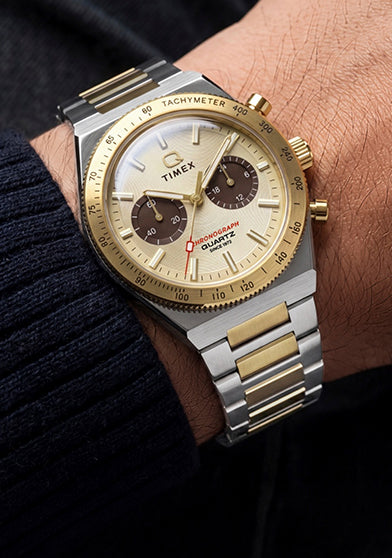 Q Timex Continental Chronograph worn on the wrist with a navy sweater, featuring a two-tone bracelet and champagne chronograph dial.