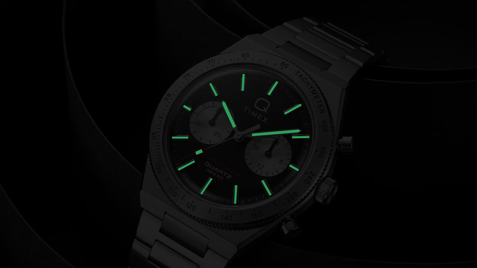 Close-up of the Q Timex Continental Chronograph in low light with green luminous hands and hour markers.