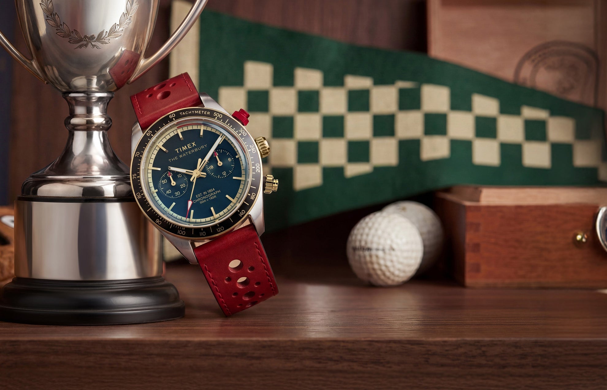 Waterbury Heritage Chronograph with blue dial and red leather strap displayed beside a silver trophy, with vintage racing-inspired decor in the background.
