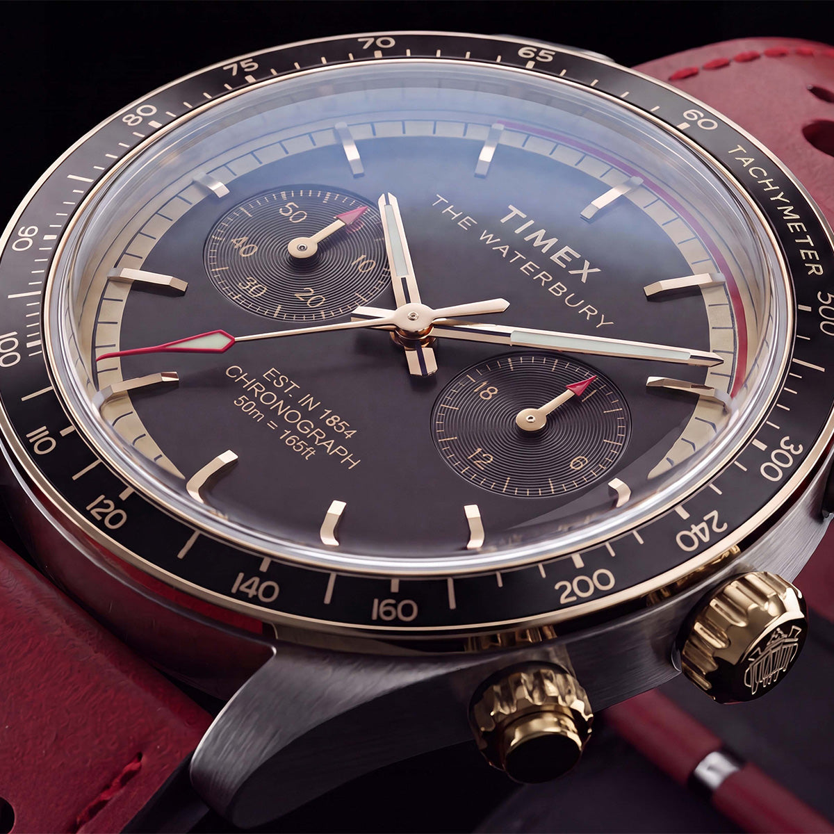Close-up of the Timex Waterbury Heritage Chronograph featuring a blue chronograph dial, contrasting sub-dials, black tachymeter bezel, and red leather racing strap.