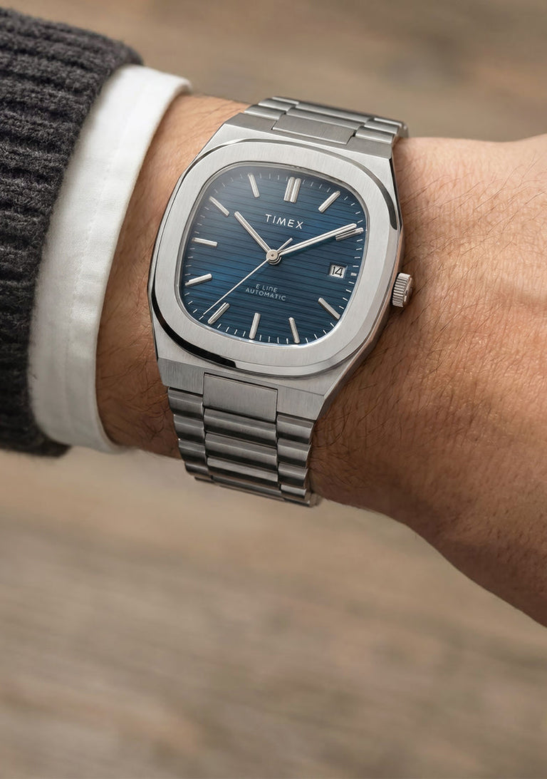 Close-up of the Timex® Automatic E Line 38mm stainless steel watch with a blue textured dial and date window worn on the wrist.